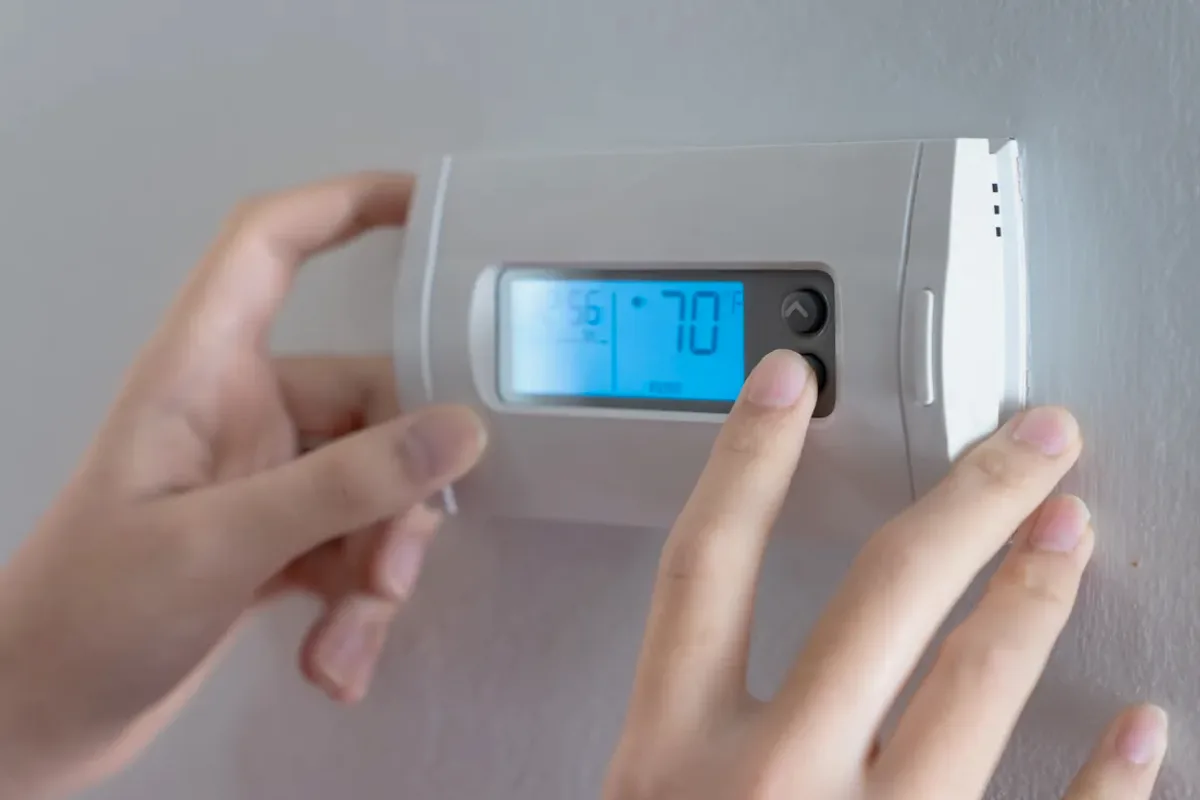 Hands adjusting a digital wall thermostat